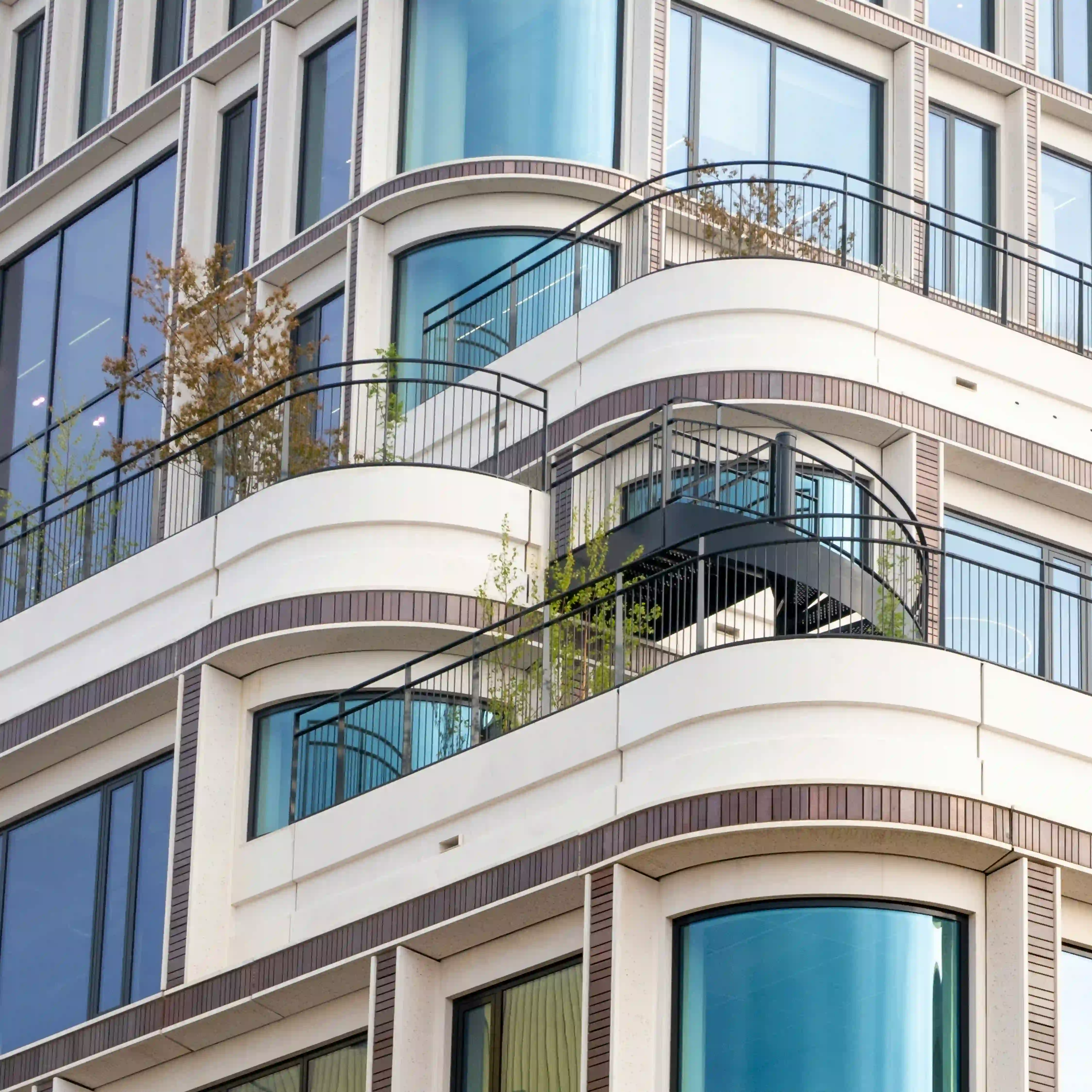 Edificio Moderno de departamentos con balcones curvos, ventanas de vidrio, barandillas de metal y plantas en las terrazas.