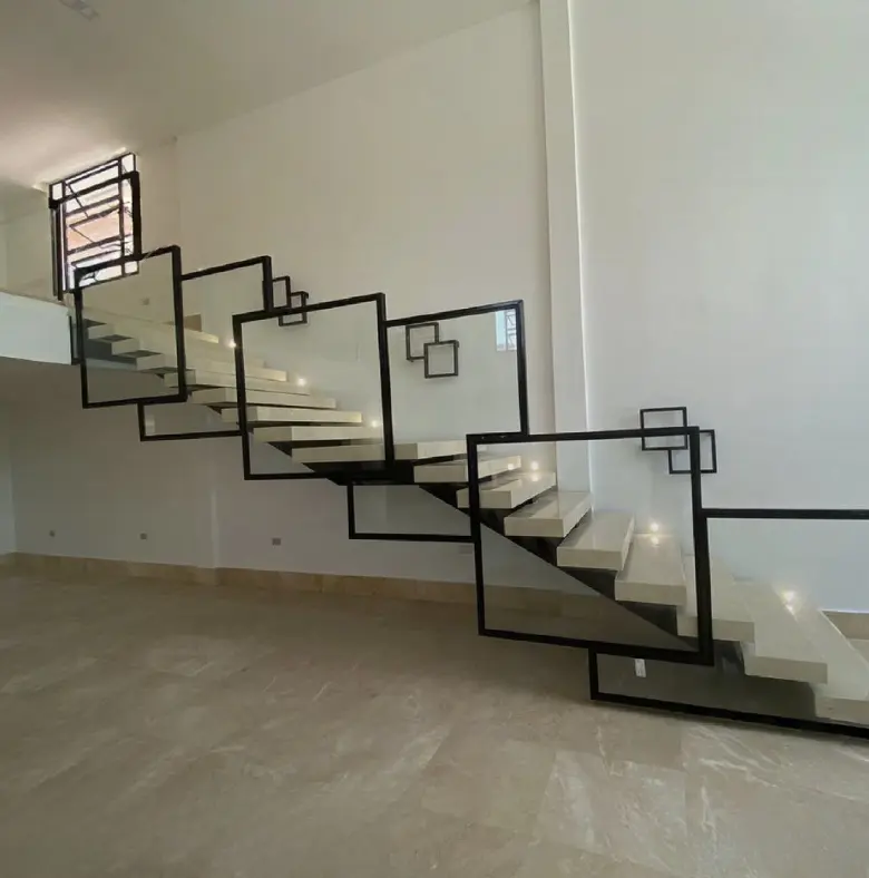 Escalera moderna flotante con barandillas de vidrio con marco negro, que conduce a una habitación luminosa y minimalista con azulejos beige.