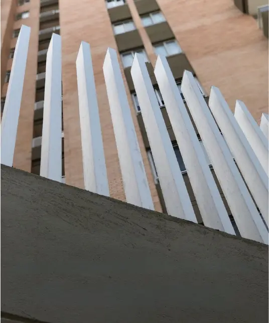 Vista hacia arriba de las lamas verticales blancas de una barandilla moderna, que contrastan con el fondo de un edificio de apartamentos de ladrillo.