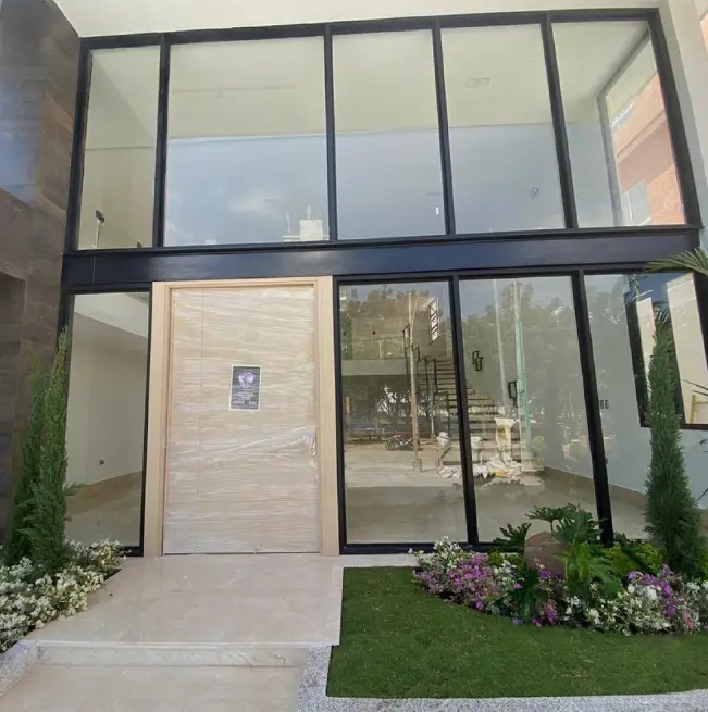 Entrada moderna de una vivienda con puerta de madera, grandes ventanas de cristal y un jardín paisajístico con flores de vivos colores.