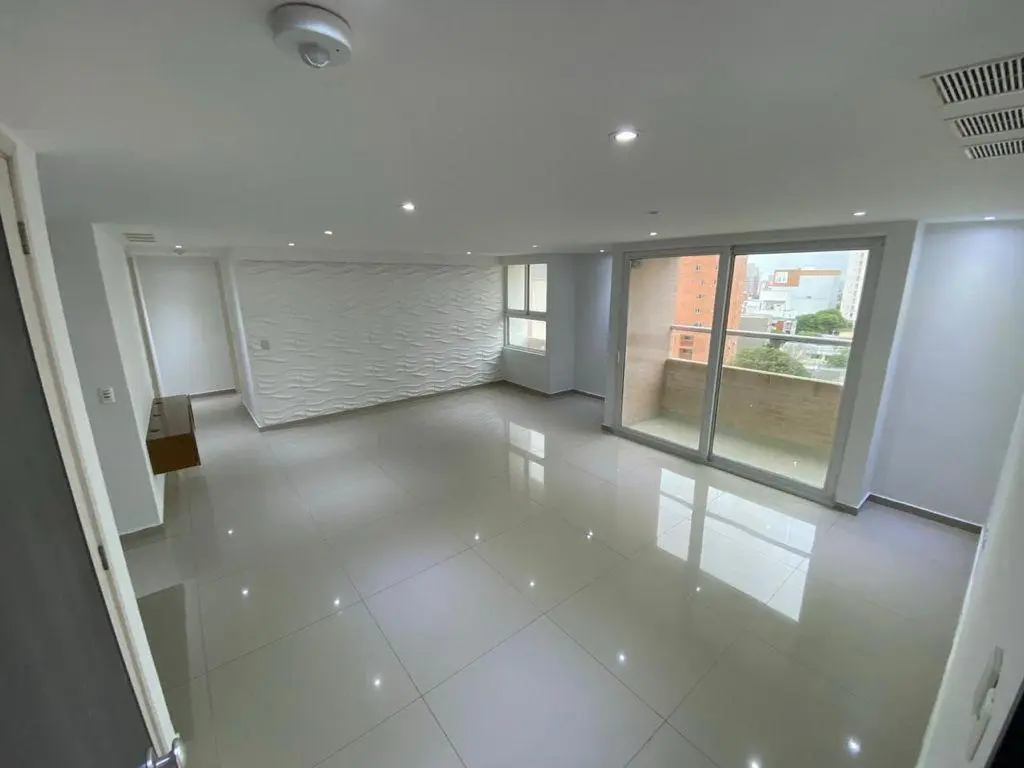 Sala de estar amplia y moderna con suelos de baldosas brillantes, paredes blancas con textura y grandes ventanas con vistas a la ciudad. Bien iluminada y acogedora.
