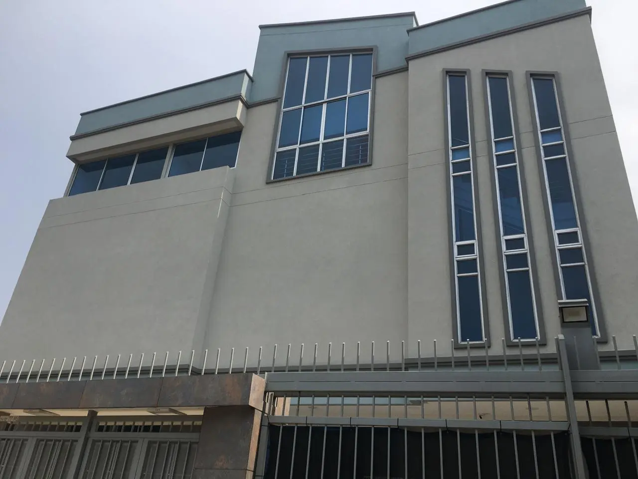 Fachada moderna con grandes ventanas de cristal y exterior gris, con diseño de ventanas verticales y una valla de seguridad en la base.